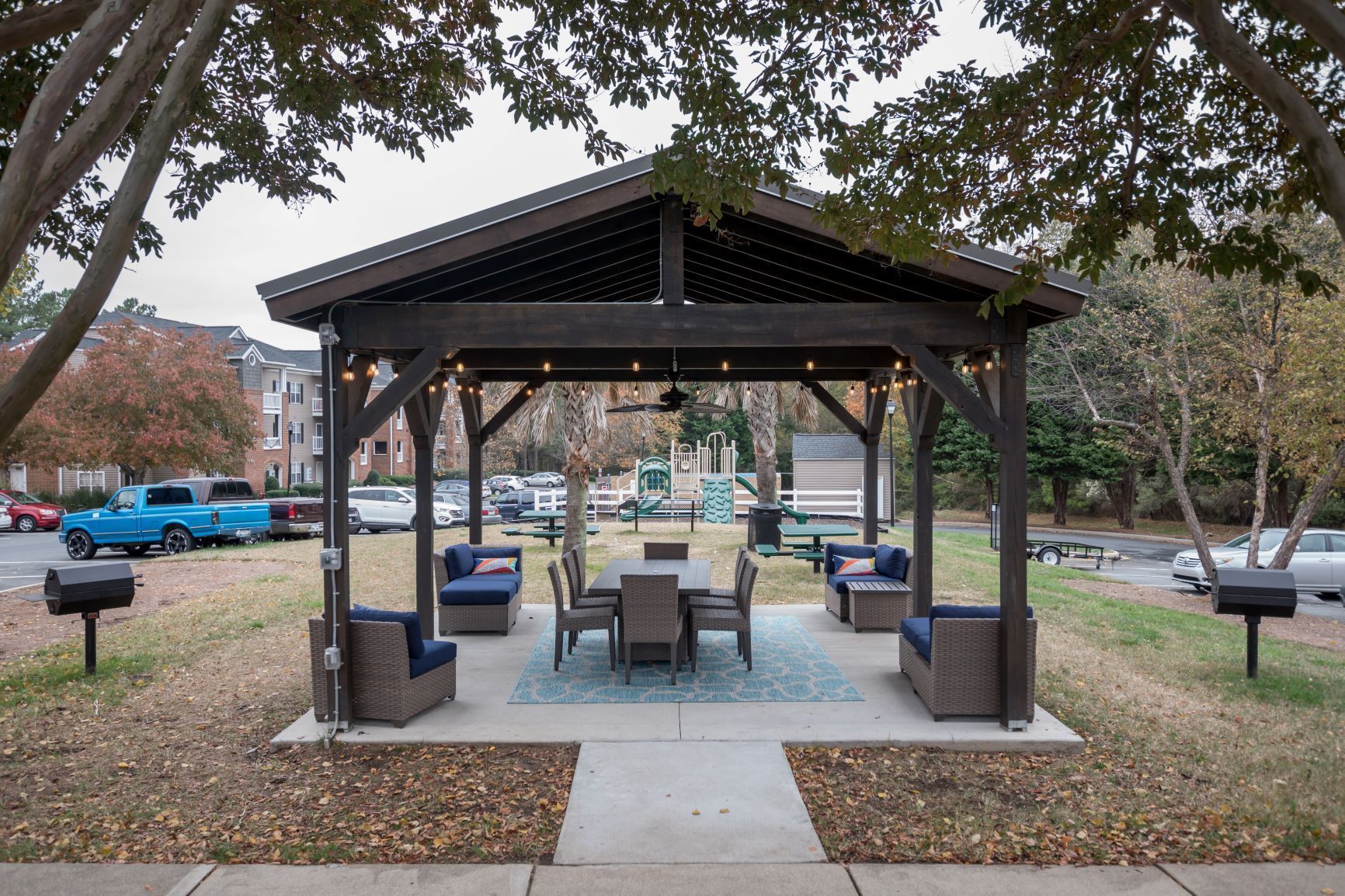 Gazebo with table and chairs in a park setting, string lights overhead.