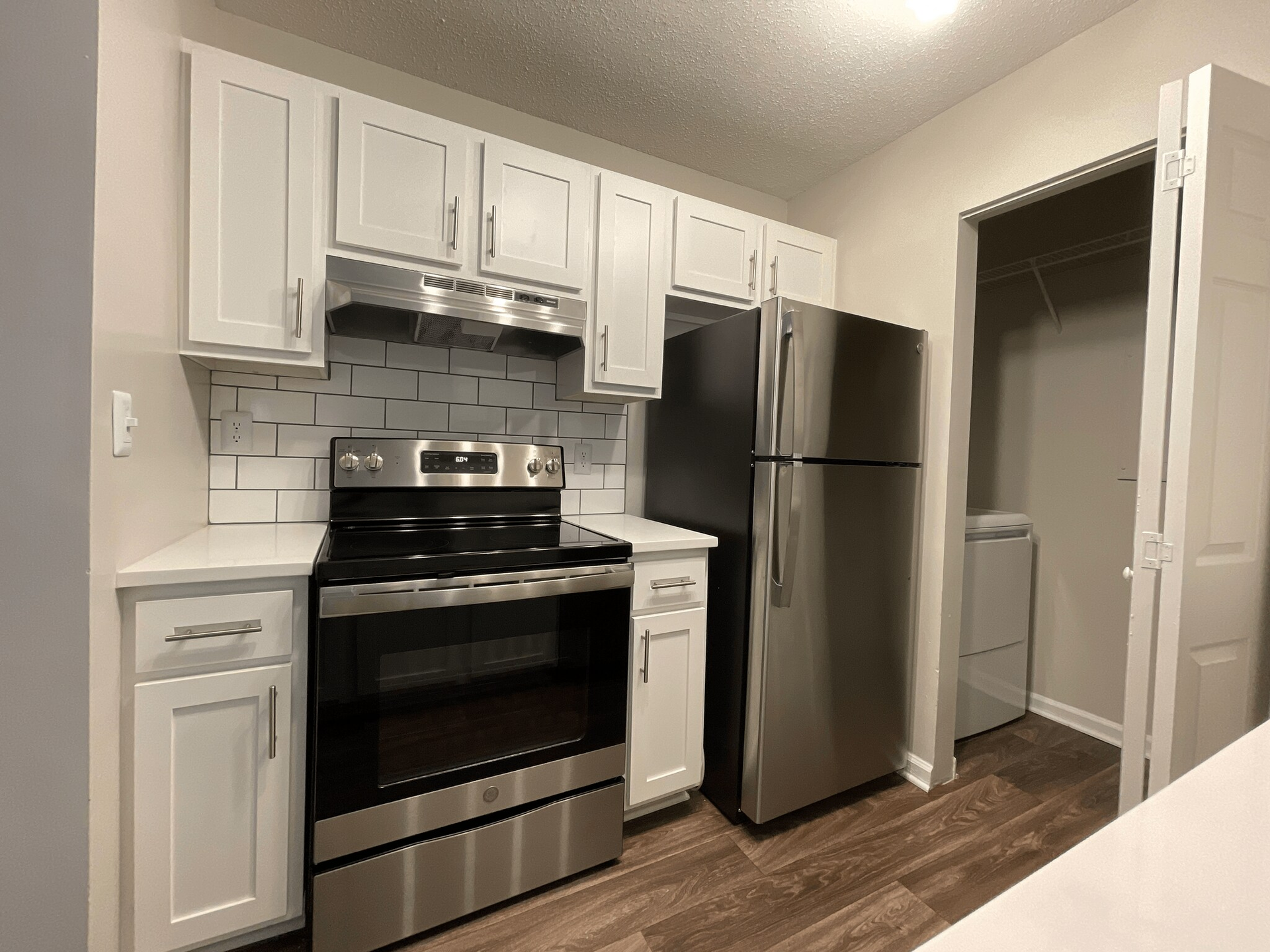 Kitchen with white cabinets, stainless steel appliances, and tile backsplash. A closet is to the right.