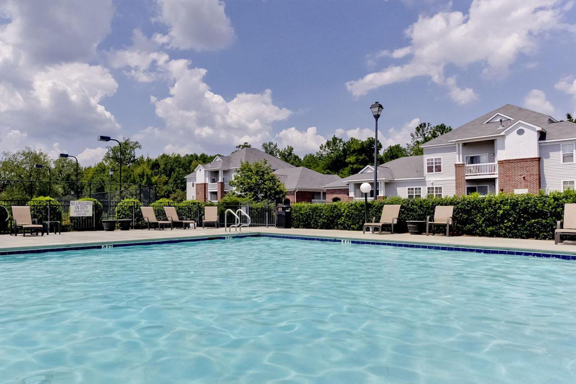 Swimming pool in front of apartment buildings on a sunny day with blue sky and chairs.