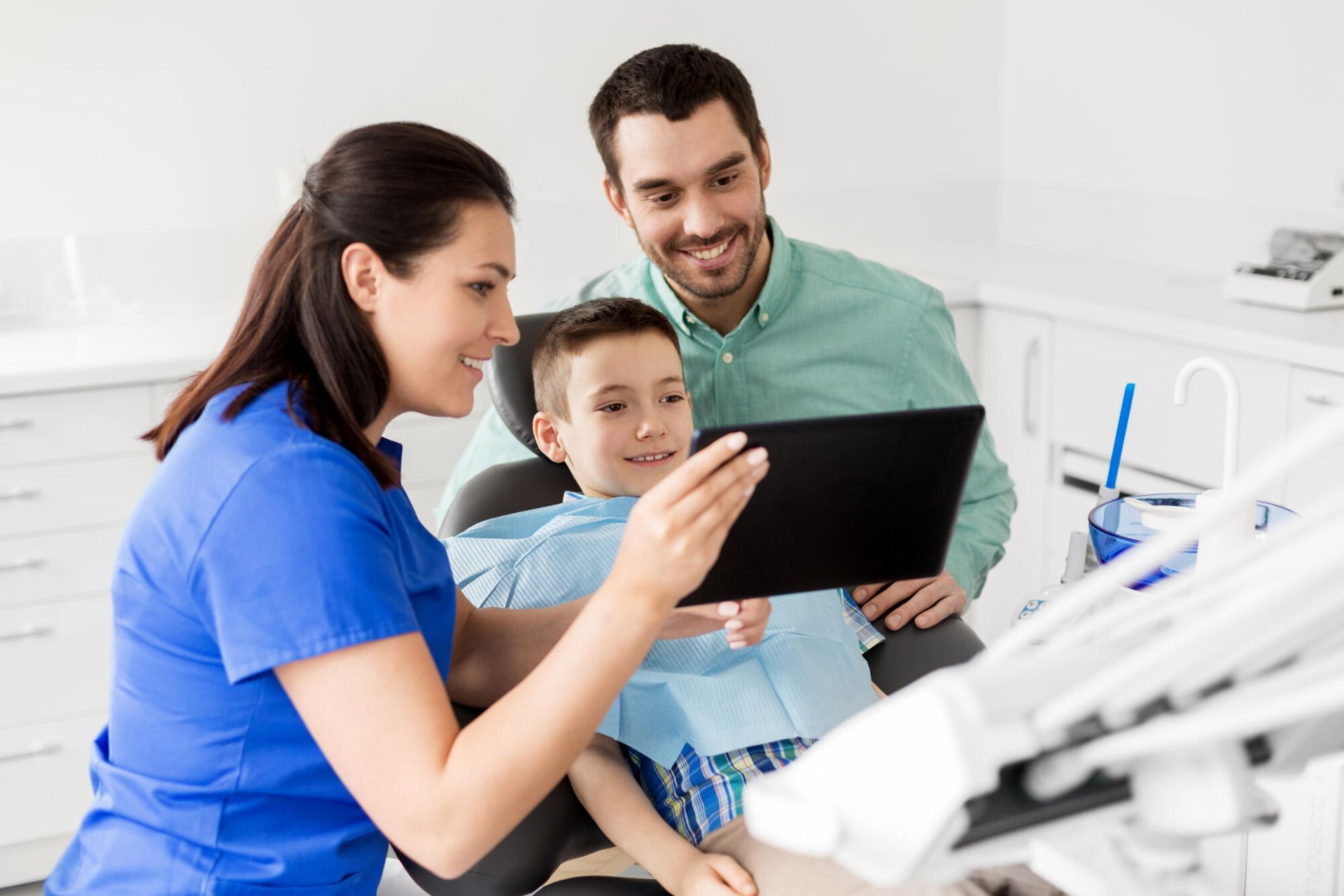 Dentist showing a child a tablet while a parent smiles in a bright dental office