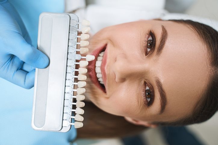 Dentist matching teeth color with a shade guide. Woman smiles in dental chair.