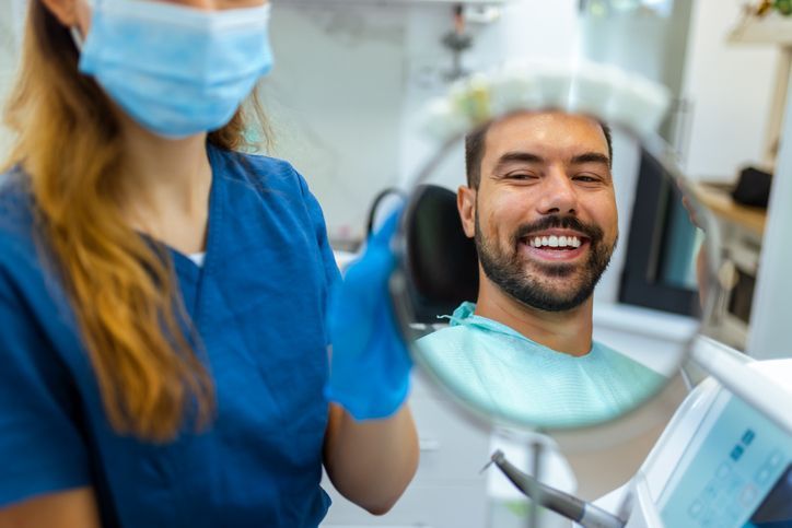 Dentist showing patient his smile in a mirror. Dentist wearing mask and gloves.