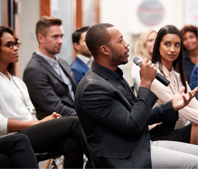 A man is speaking into a microphone in front of a group of people