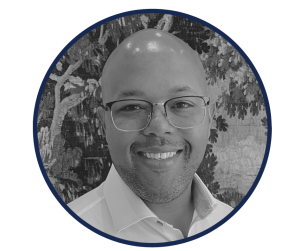 A man wearing glasses and a white shirt is smiling in a black and white photo.