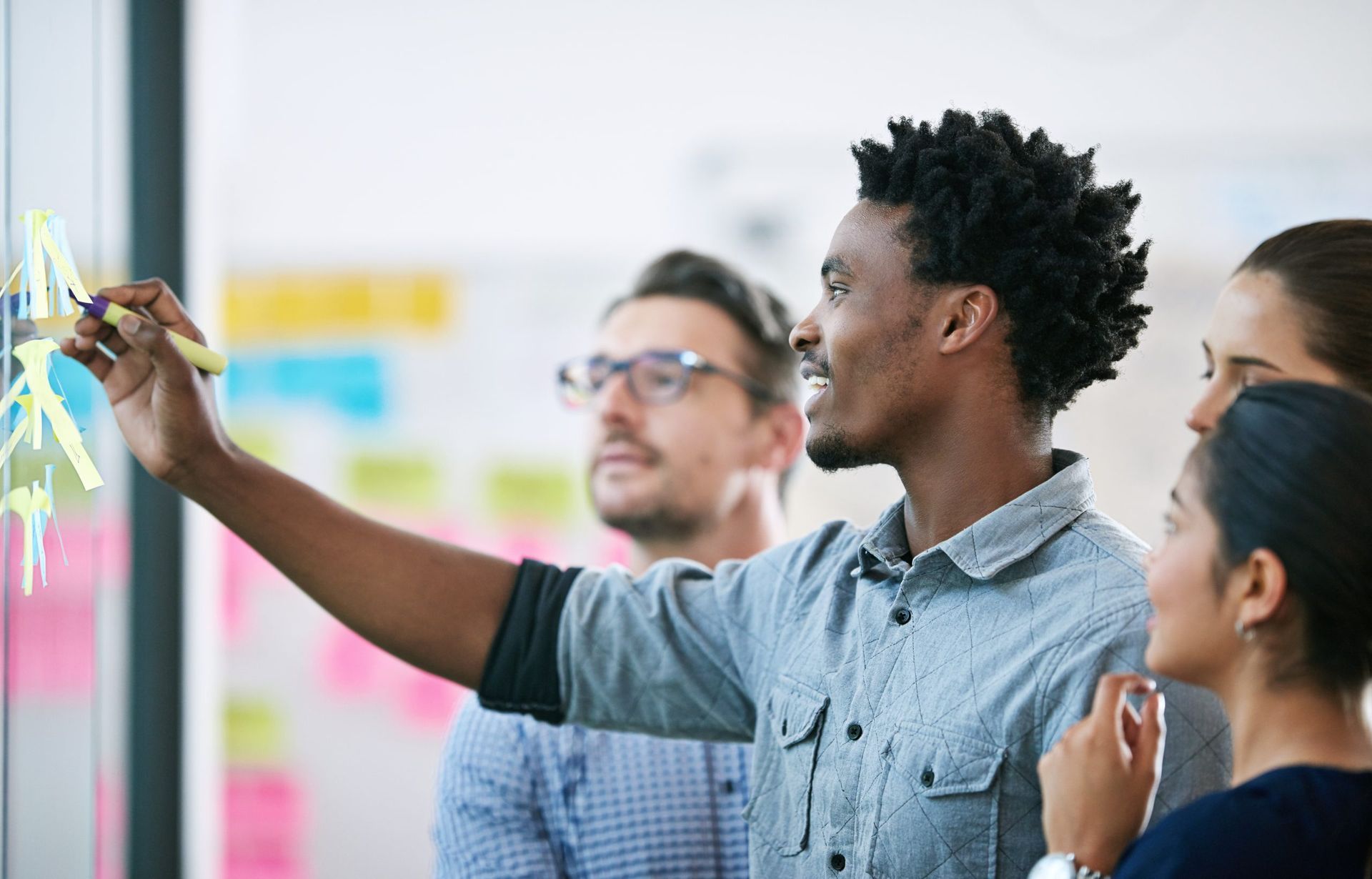 A man is writing on a whiteboard with sticky notes while a group of people look on.