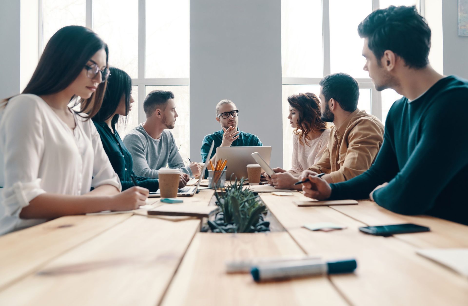 A group of people are sitting around a wooden table having a meeting.