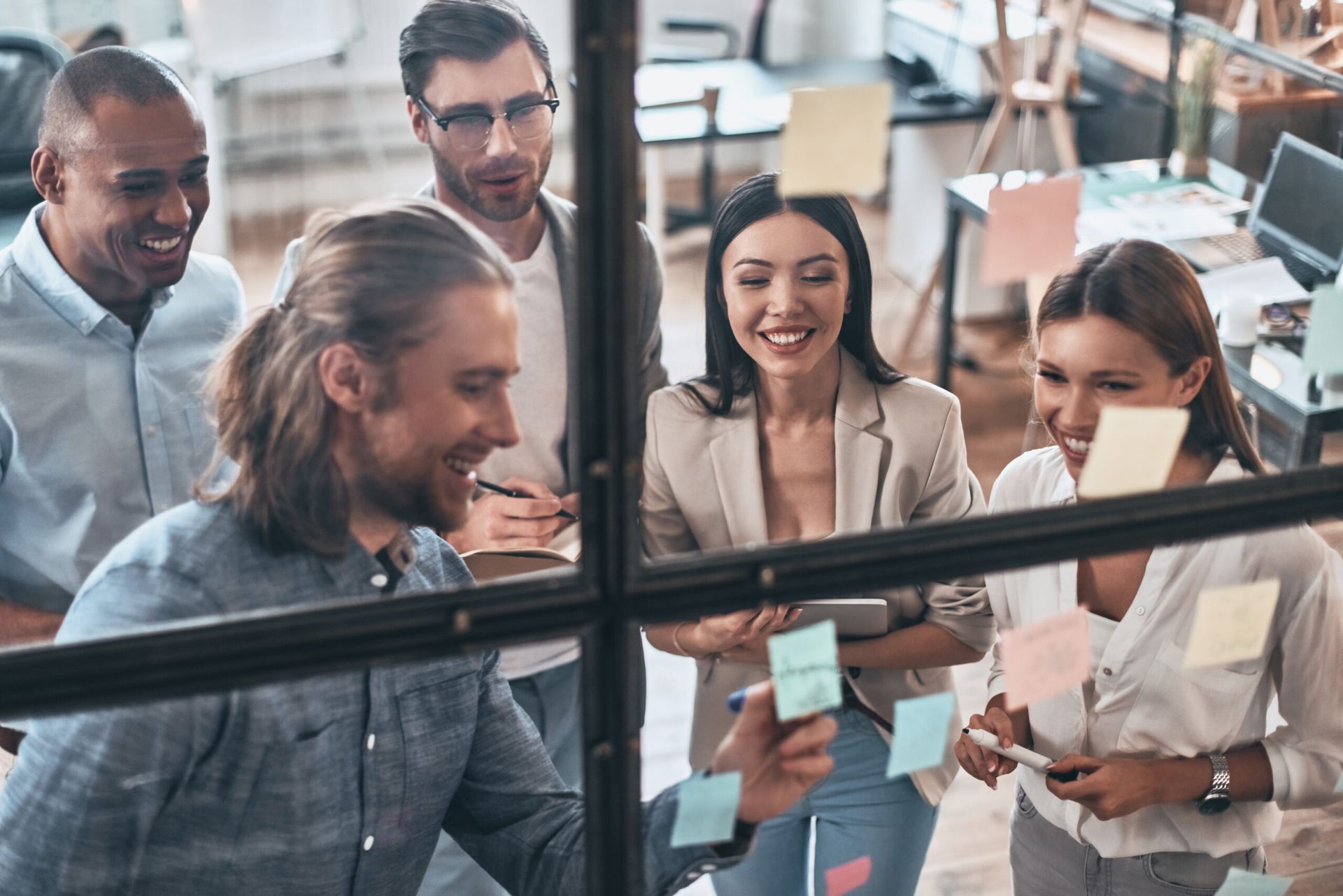 A group of people are standing around a glass wall with sticky notes on it.