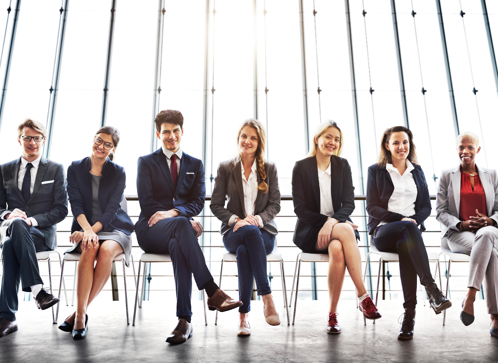 A group of business people are sitting in a row in front of a window.