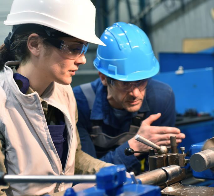 A man and a woman wearing hard hats are working on a machine