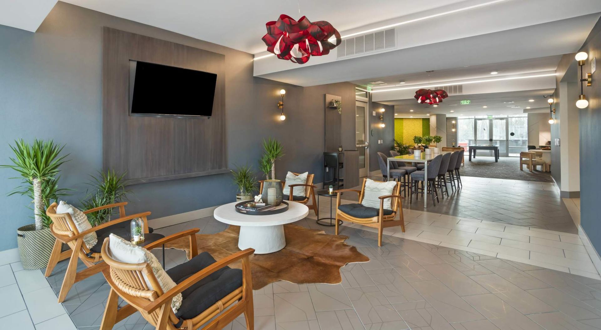 Interior community lounge with modern seating, a wall-mounted TV, and potted plants.