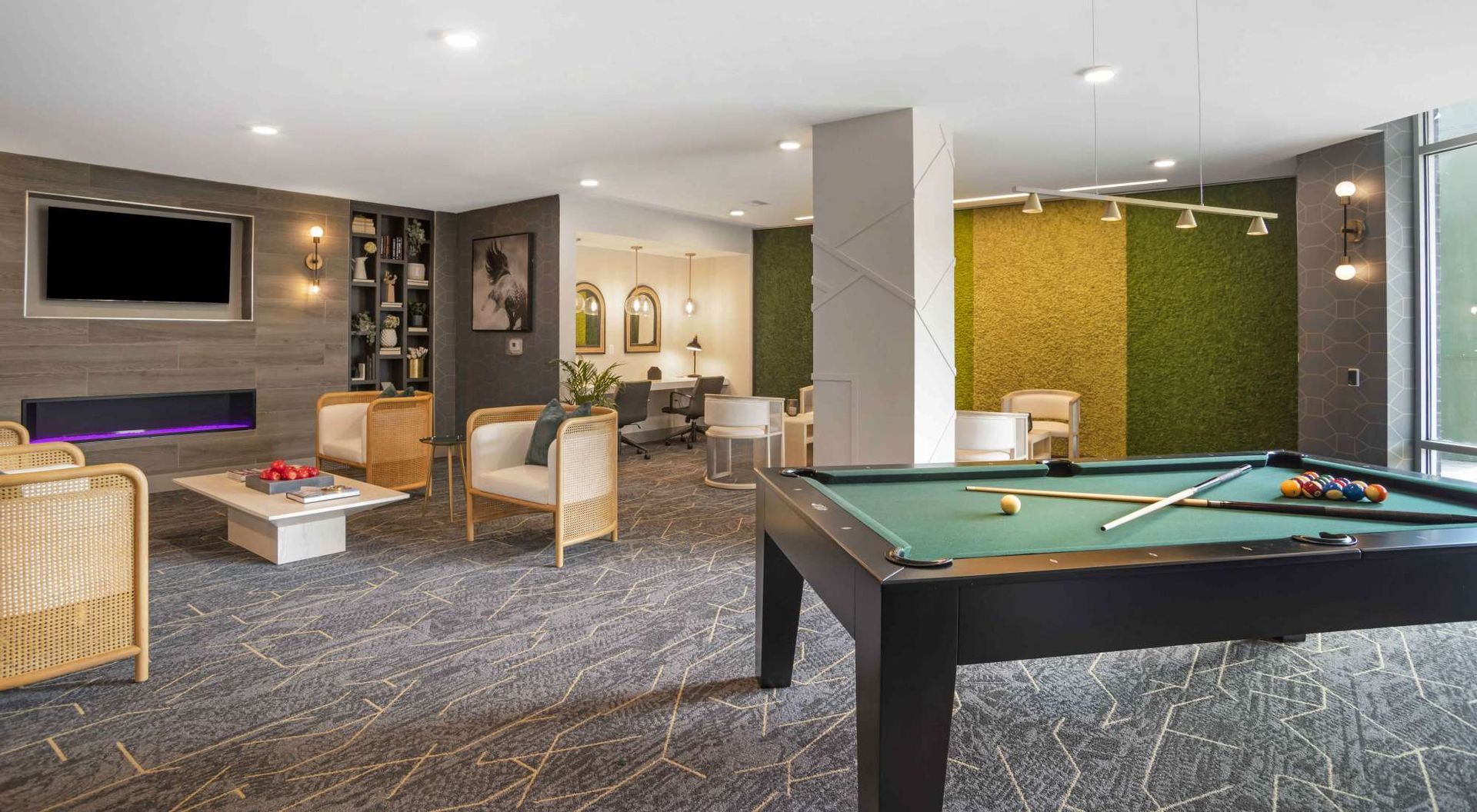 Modern resident lounge with a pool table, seating area, bookshelf wall, and a fireplace.