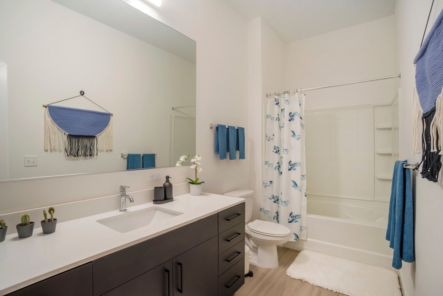 Modern bathroom with dark vanity, white countertop, toilet, and a tub/shower with a blue fish-pattern curtain.