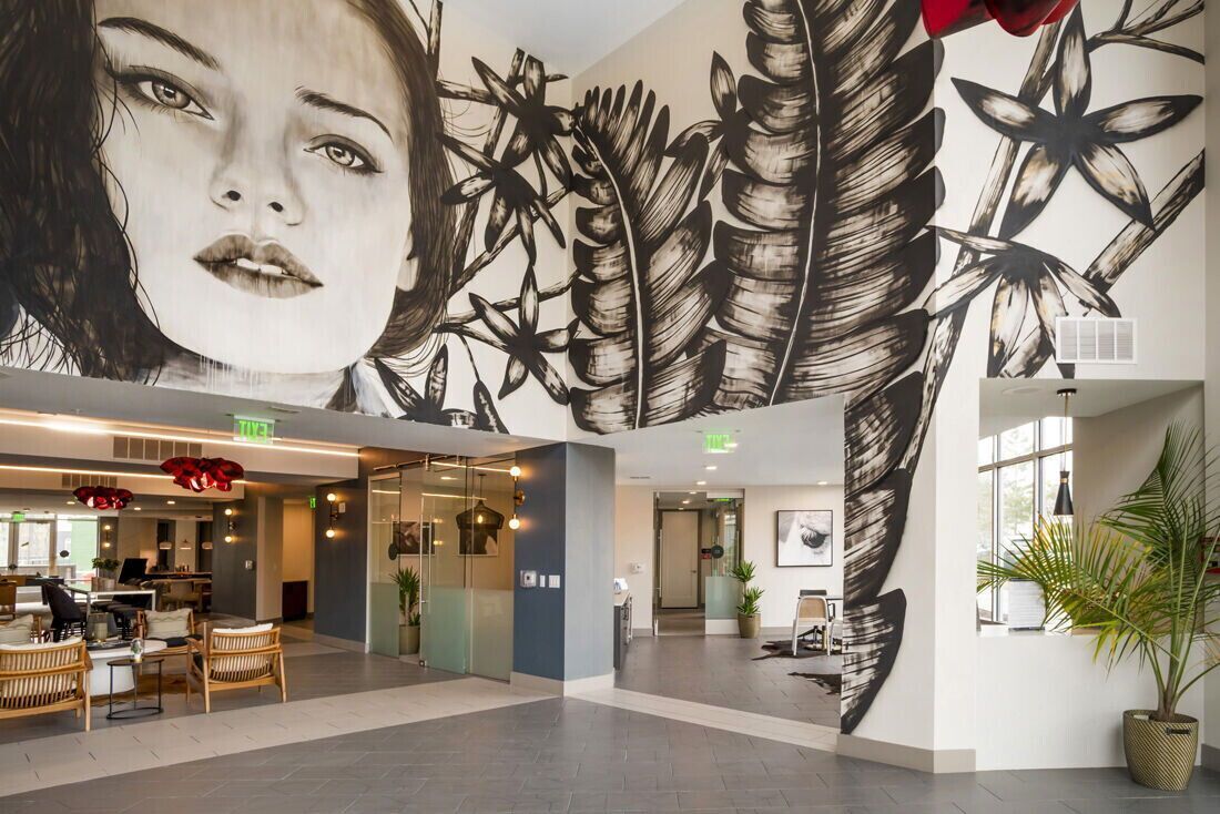 Indoor apartment lobby with a large black-and-white mural, seating, and plants.
