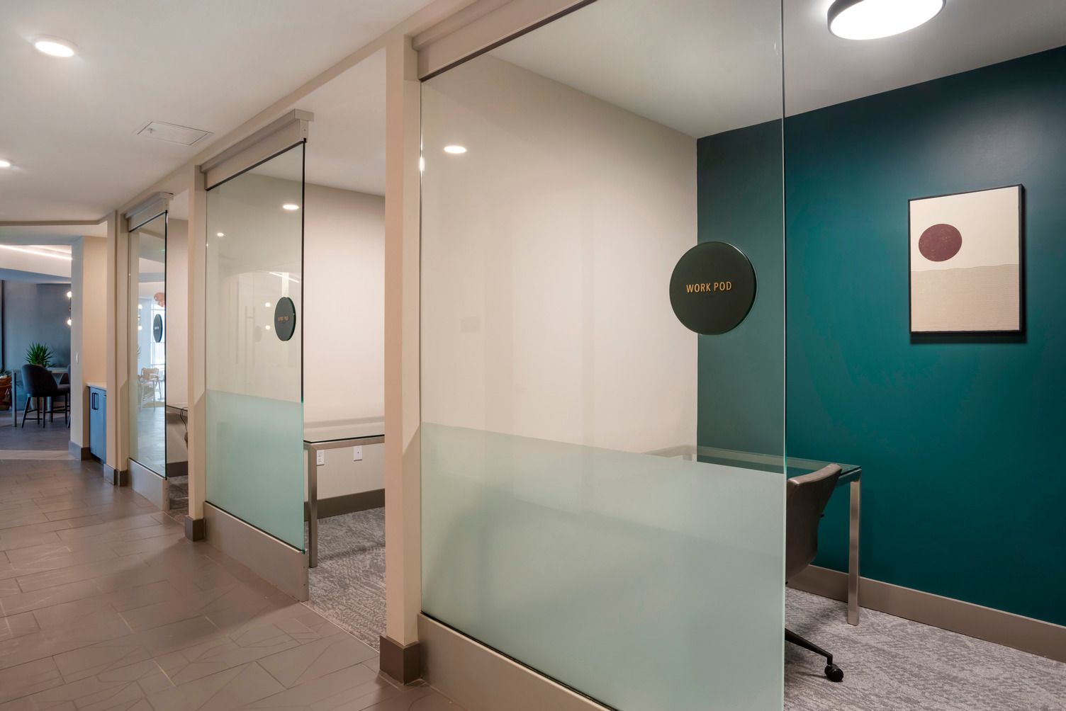 Interior hallway with glass partitions and a frosted work pod; teal accent wall.