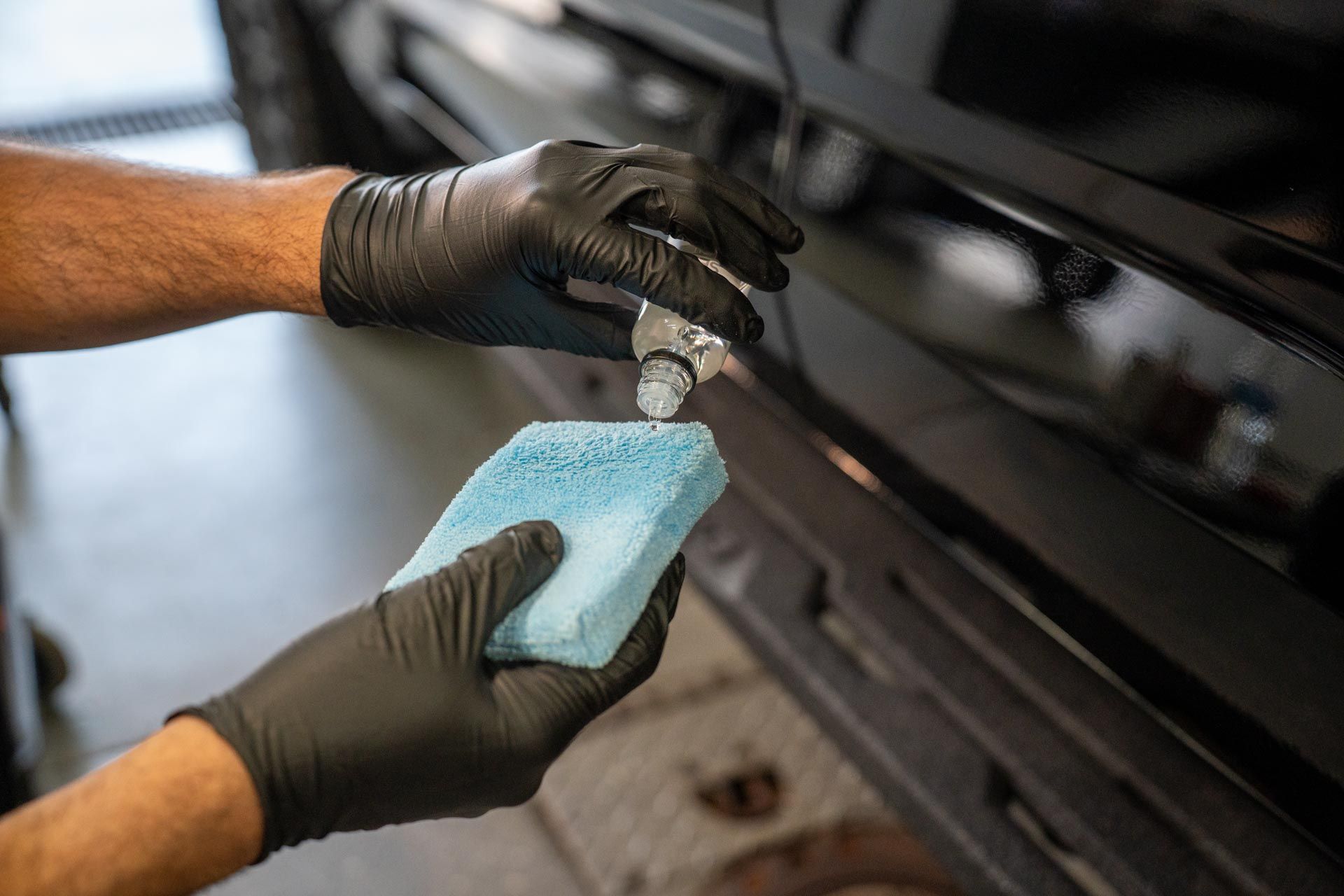 A man wearing black gloves is cleaning a car with a blue sponge.