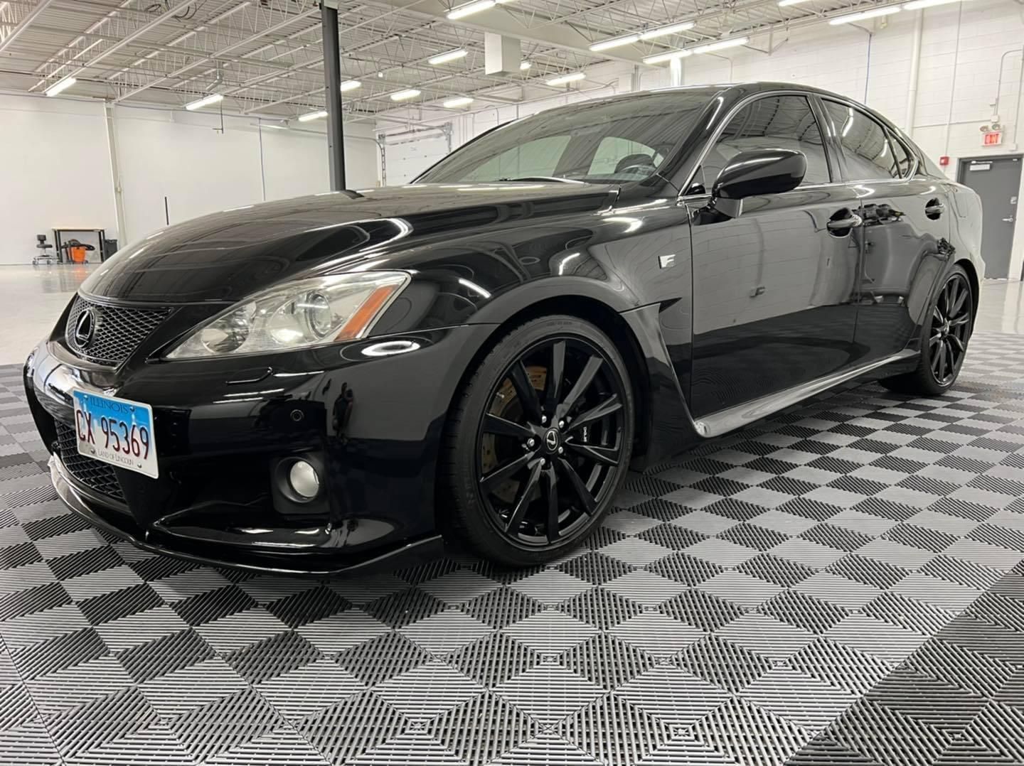 A black car is parked on a checkered floor in a garage.