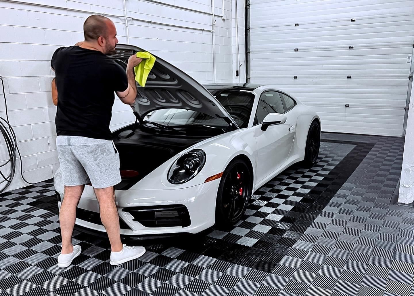 A man is cleaning a white sports car with a towel in a garage.