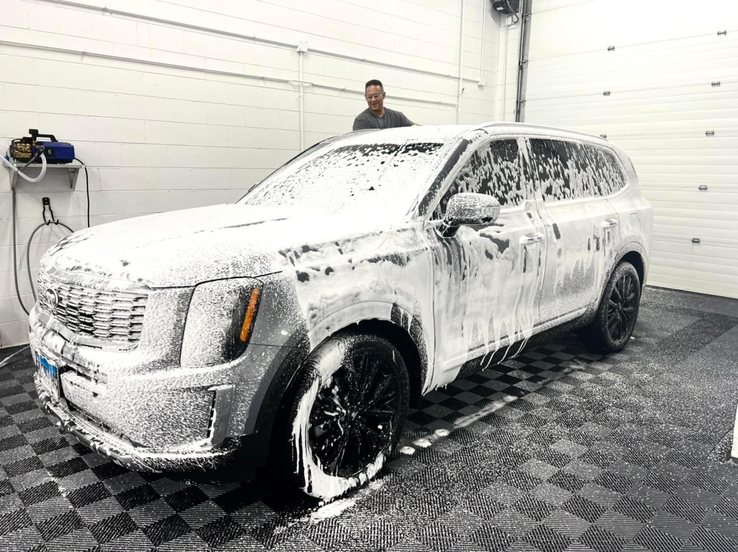 A man is standing next to a white suv covered in foam.