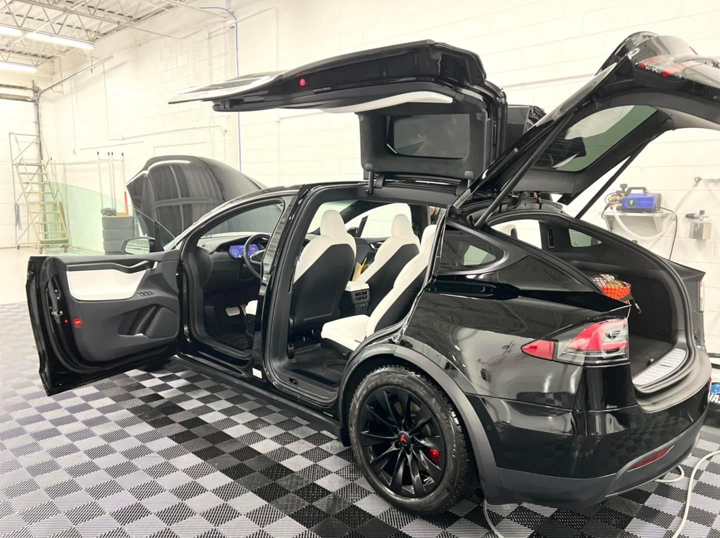 A black tesla model x with its doors open is parked in a garage.