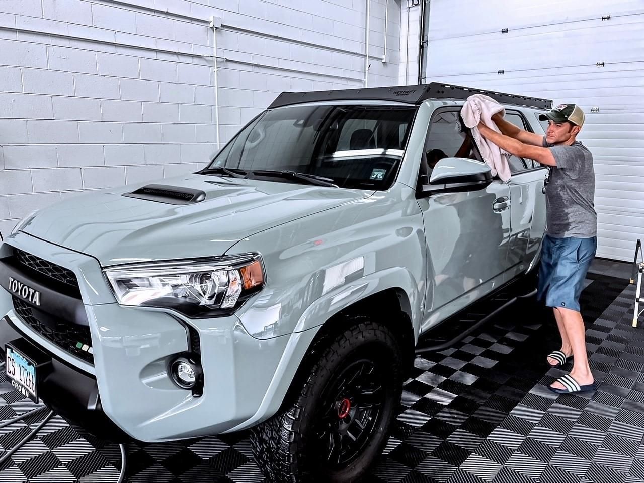 A man is cleaning a gray truck with a towel in a garage.