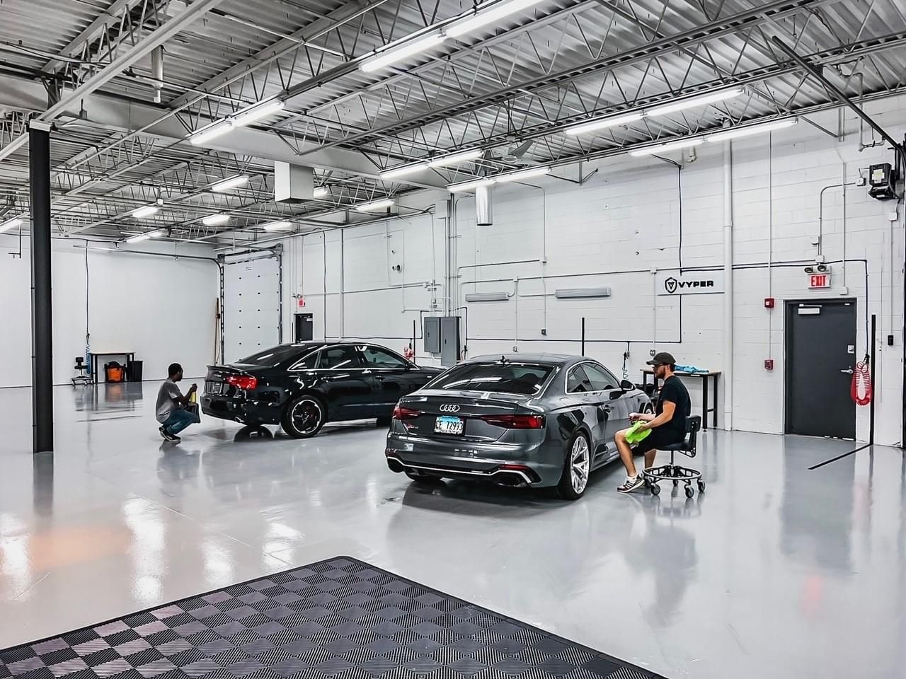 A man is sitting in a chair in a garage next to a car.
