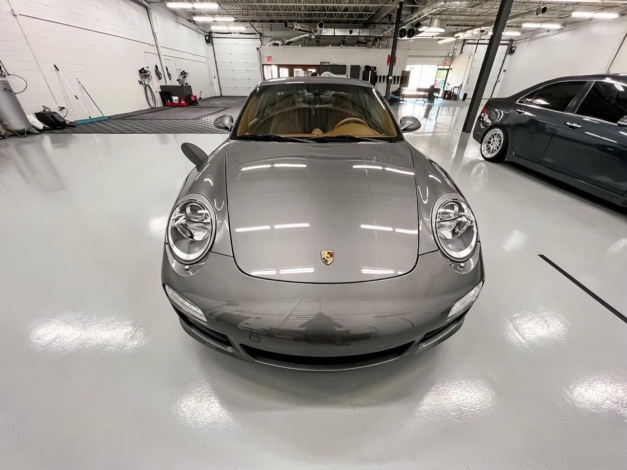 A gray porsche 911 is parked in a garage.