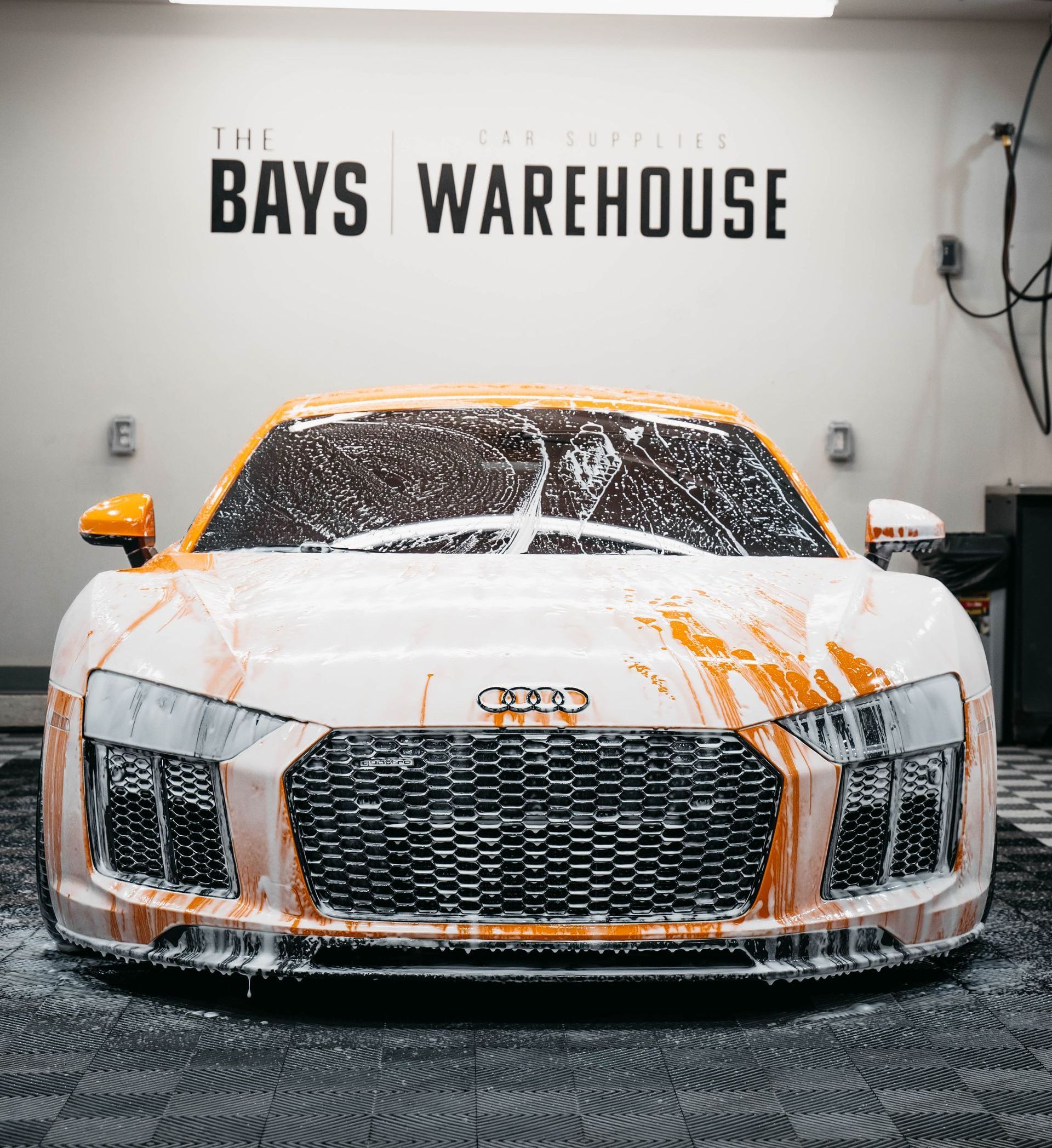 A white and orange sports car is covered in foam in a garage.