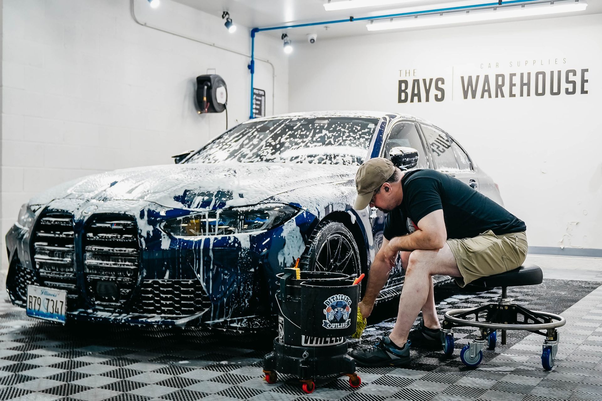 A man is sitting on a stool washing a car in a garage.