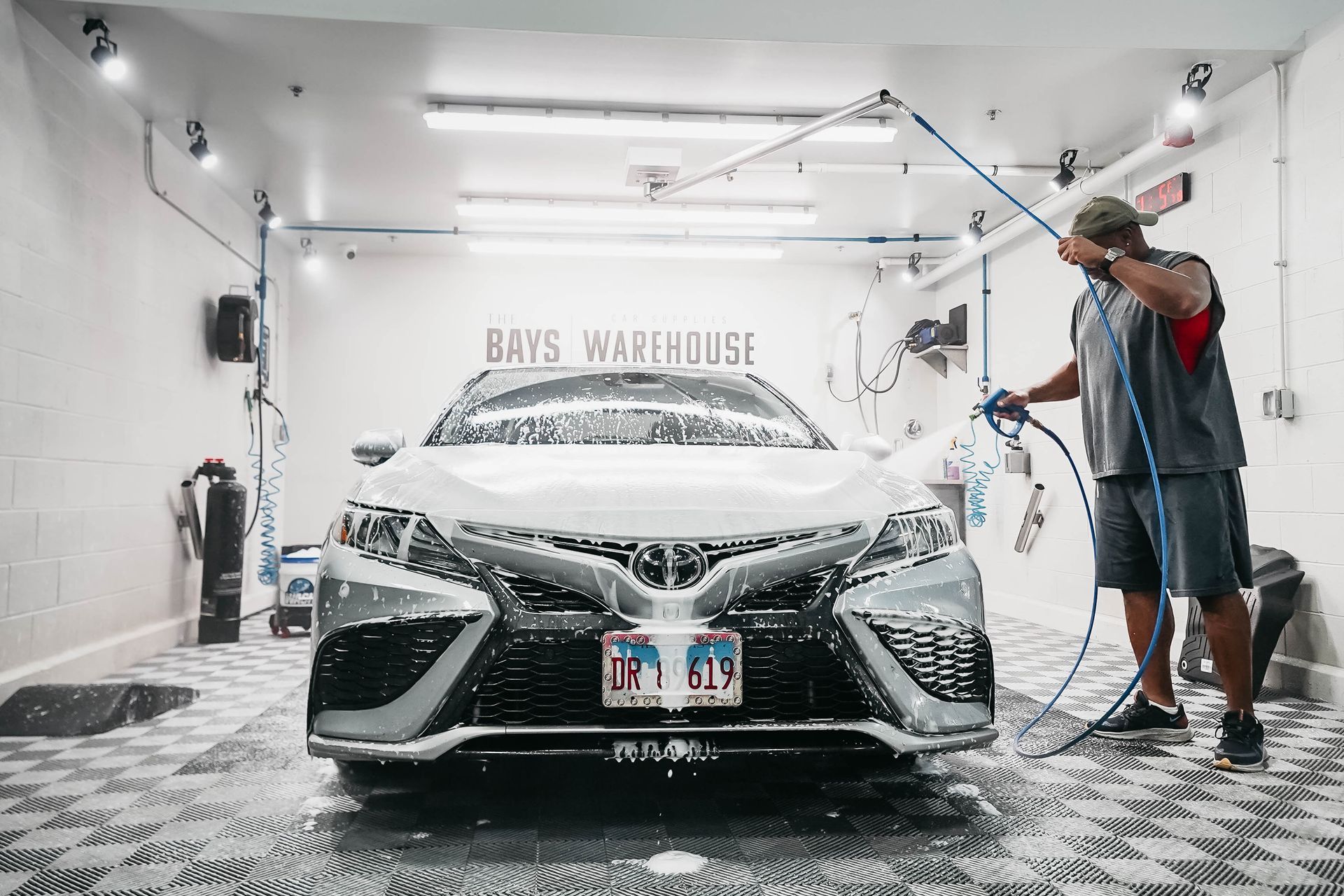 A man is washing a white car in a garage.