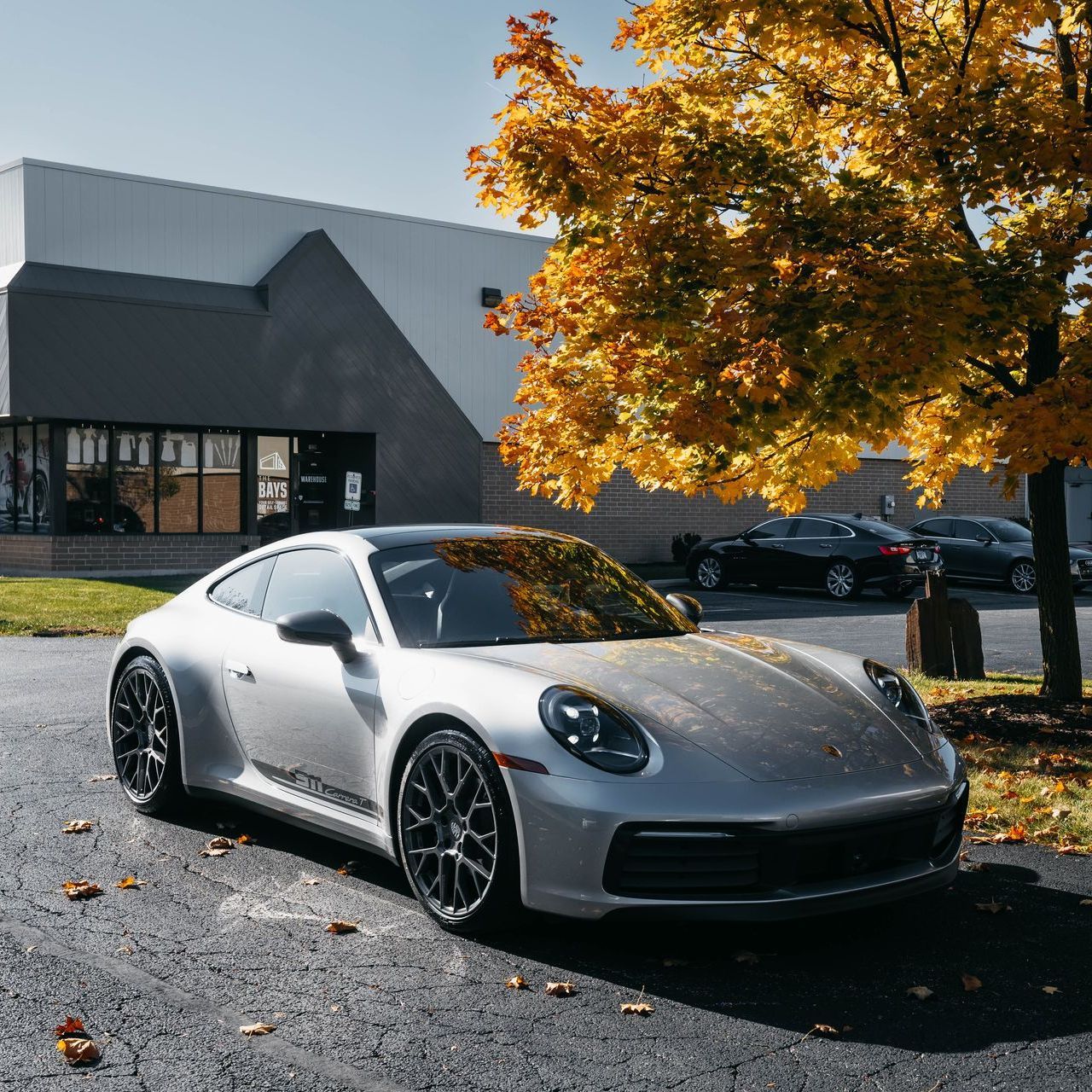 A silver porsche 911 is parked in front of a building
