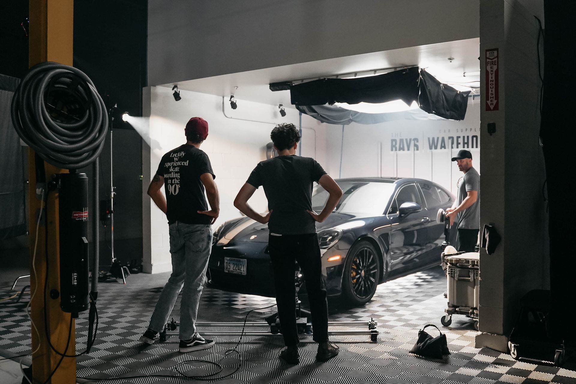 Two men are standing next to a car in a garage.
