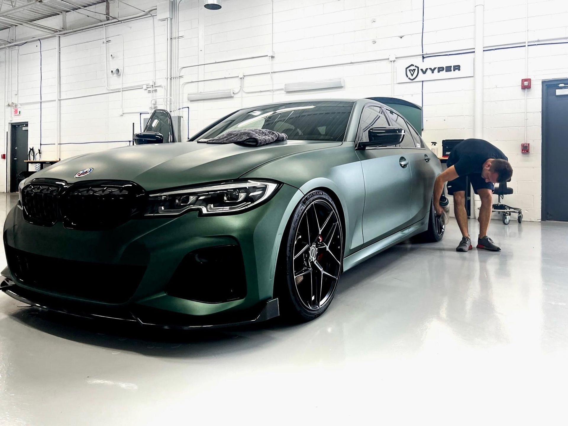 A man is standing next to a green bmw in a garage.