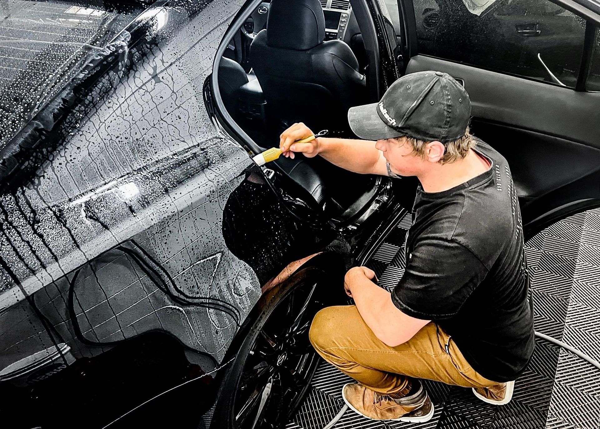 A man is cleaning the hood of a black car with a brush.