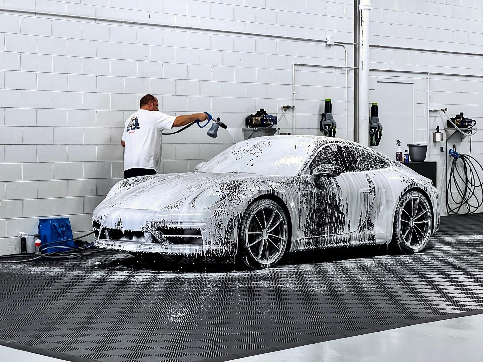 A man is washing a car with foam in a garage.
