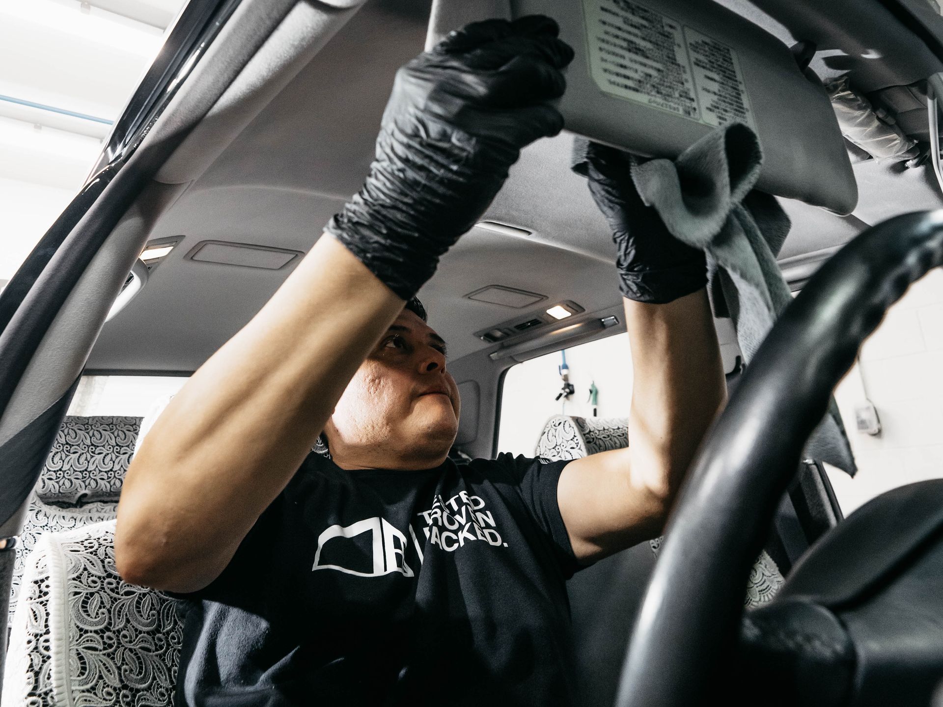 A man wearing black gloves is working on the roof of a car.