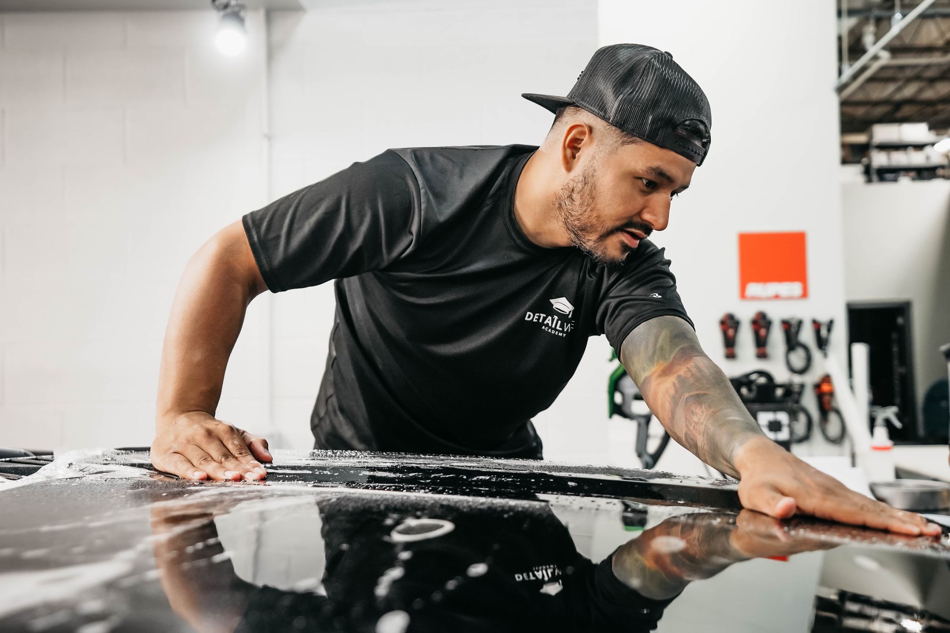 A man is cleaning the hood of a car in a garage.