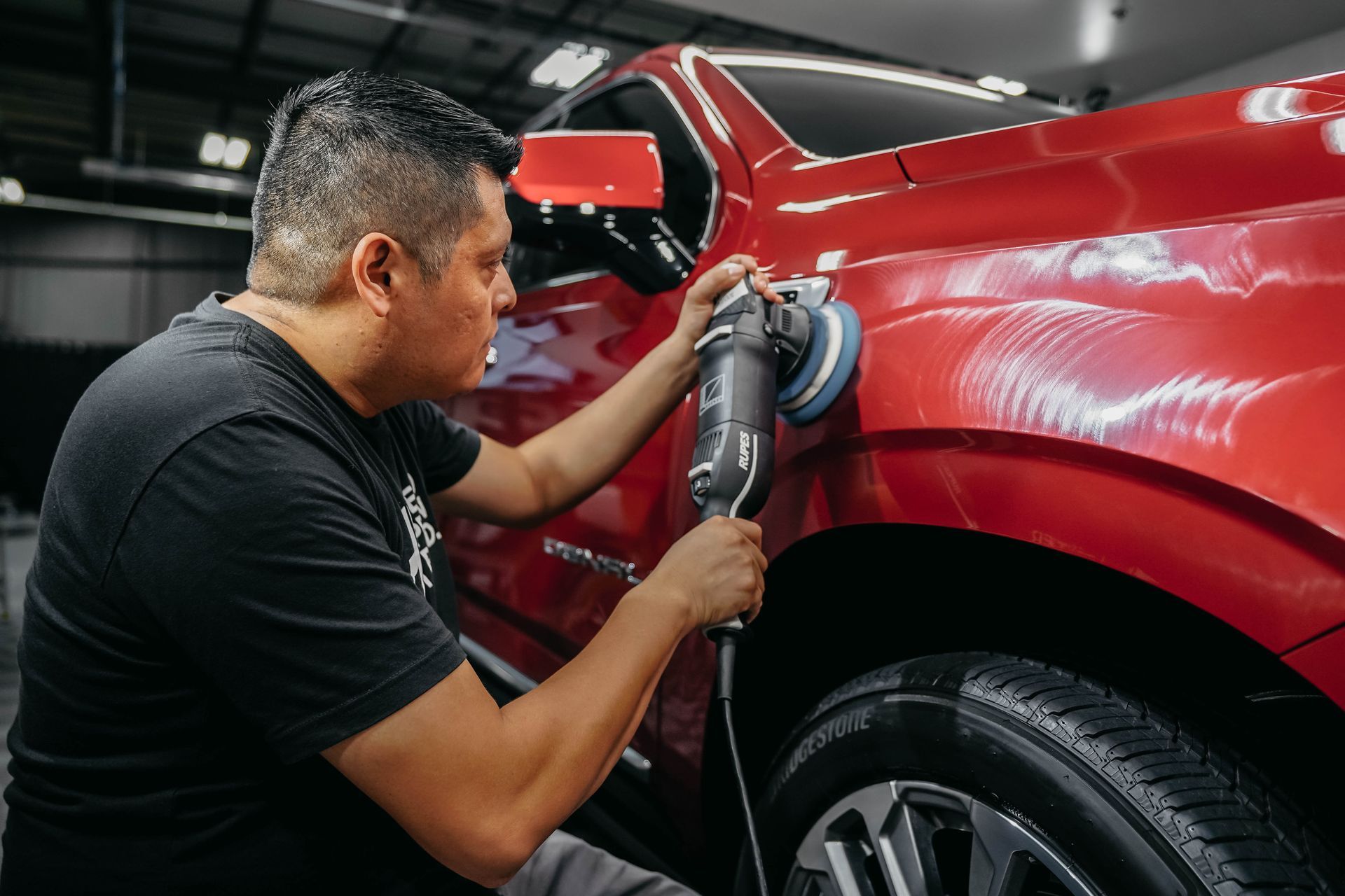 A man is polishing a red car with a machine.