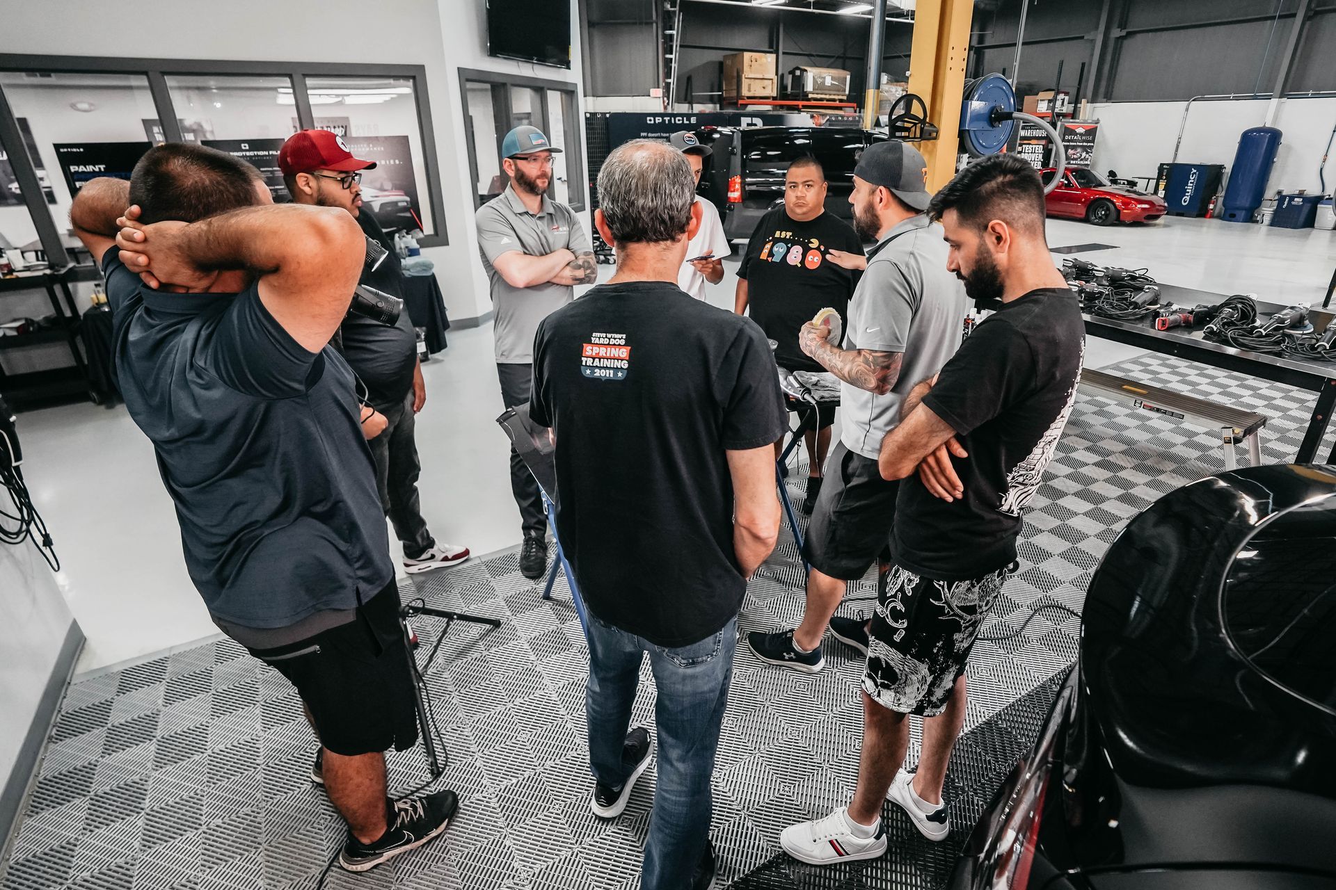 A group of men are standing in a circle in a garage talking to each other.