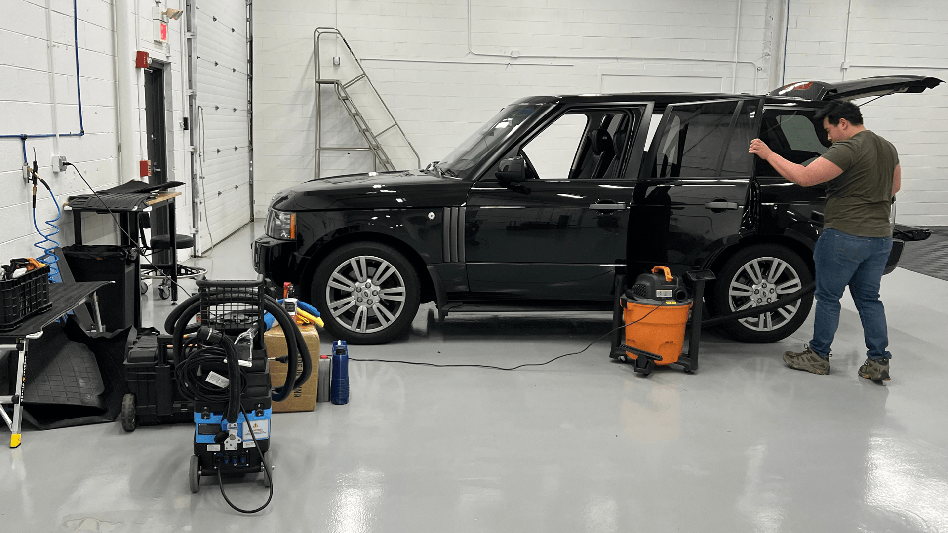 A man is cleaning the windows of a black range rover in a garage.