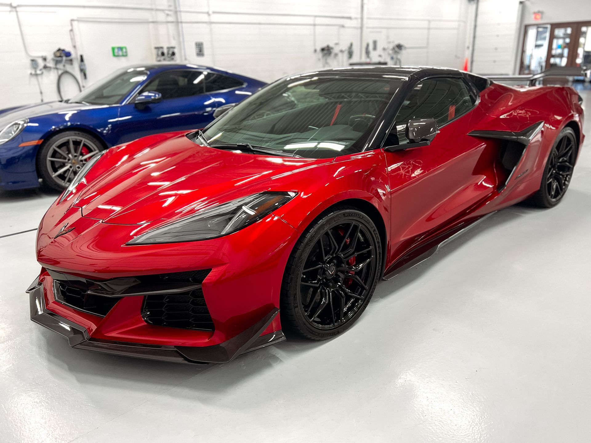 A red sports car is parked next to a blue sports car in a garage.