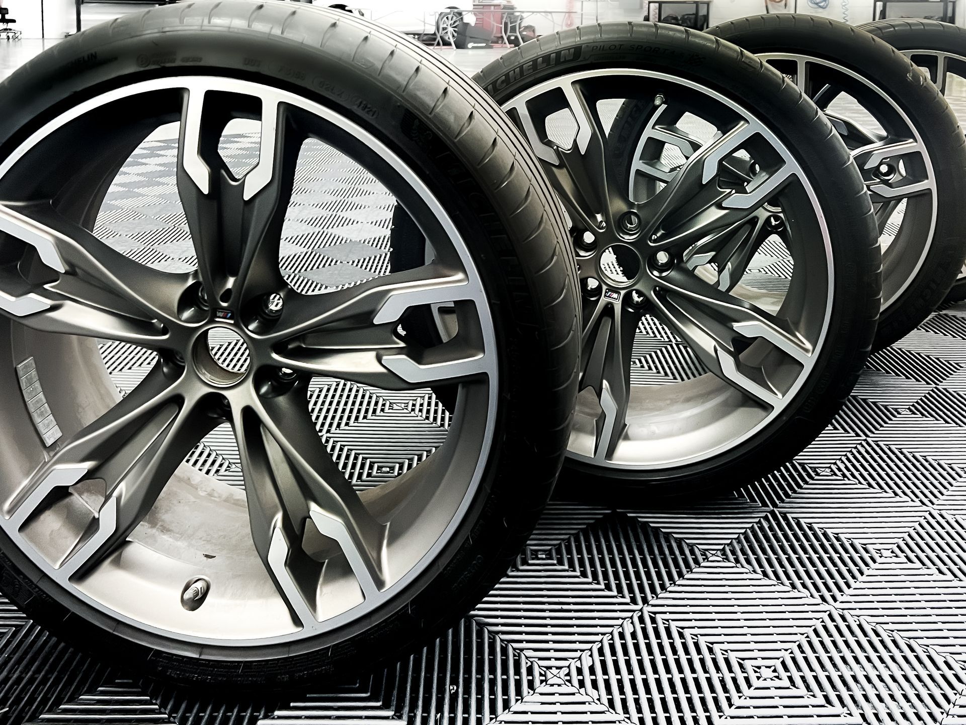 A row of wheels and tires are sitting on a tiled floor.