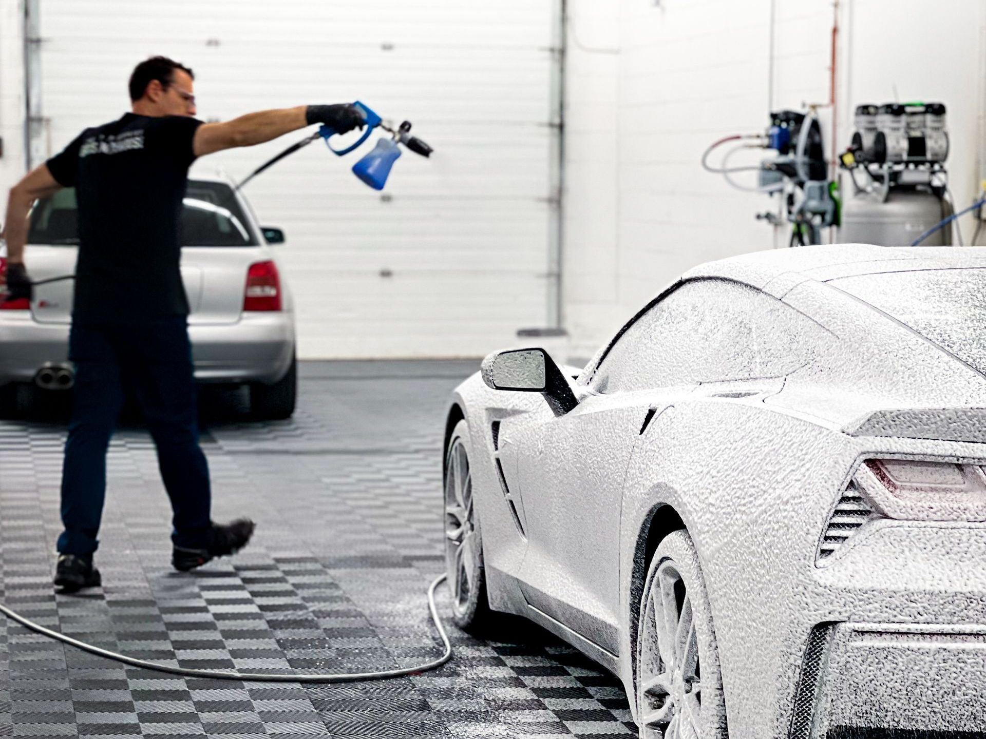 A man is washing a white sports car in a garage.