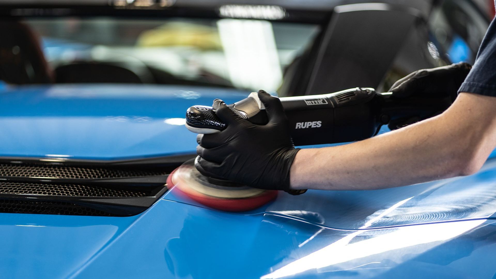A person is polishing the hood of a blue car.