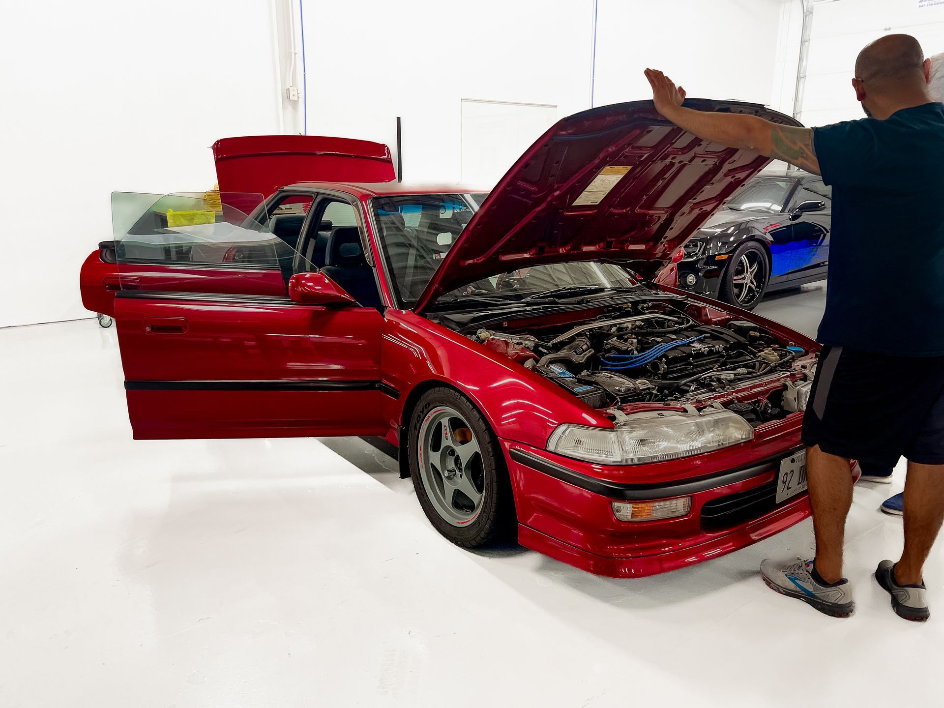 A man is standing in front of a red car with the hood open.