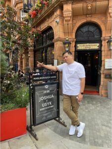 A man is standing in front of a building pointing at a sign.