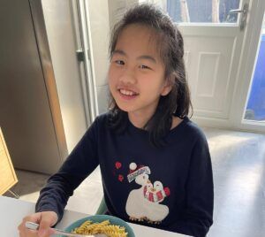 A little girl is sitting at a table eating pasta with a fork.