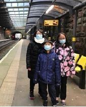 A group of people wearing face masks are standing on a train platform.