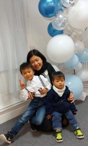 A woman is sitting on the floor with two children in front of balloons.