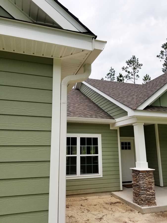 A green house with a porch and a white gutter