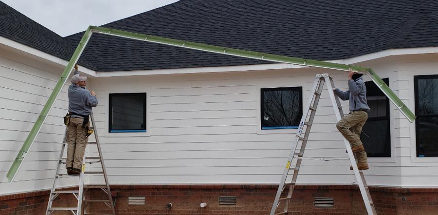 Two men are standing on ladders painting the side of a house.
